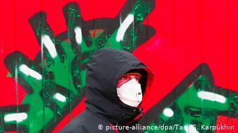 Человек в маске на фоне рисунка на стене, изображающего коронавирус