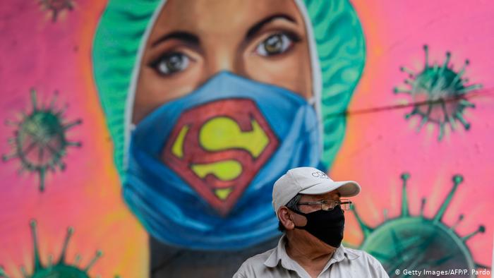 Граффити: женщина-медик в хирургической шапочке и маске с символом супермена. На фоне граффити стоит мужчина в защитной маске.