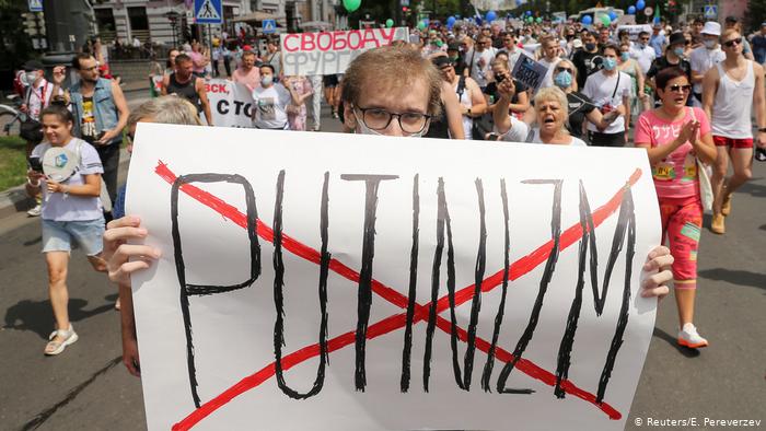 Один из участников протестов в Хабаровске держит в руках плакат, на котором красным крестом перечеркнуто слово Putinizm.