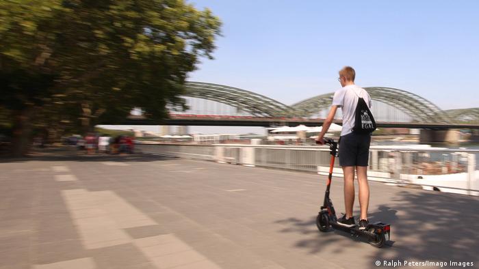 Подросток едет на электроскутере по набережной Рейна в Кельне
