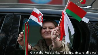 Девушка в окне машины держит в руках два белорусских флага: официальный и бело-красно-белый
