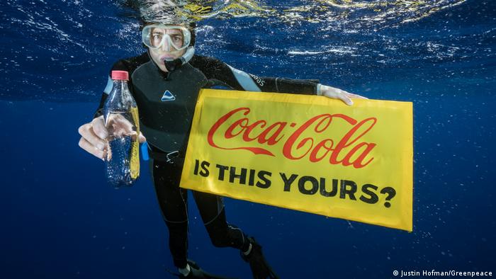 В руках активиста под водой транспарант и бутылка из под Кока-Колы