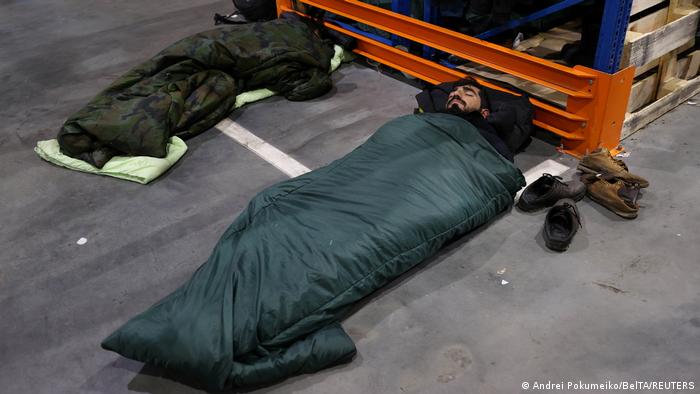 Мигранты в спальных мешках спят на полу в центре для их размещения. 