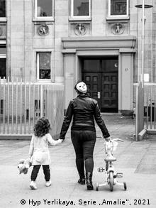 Женщина с ребенком и трехколесным велосипедом подходит к зданию