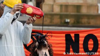 Человек льет жидкость, изображающую топливо, на лицо демонстранта, показывая таким образом негативное отношение к нефтегазовой индустрии