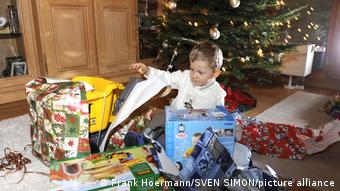 Ребенок распаковывает подарки под елкой