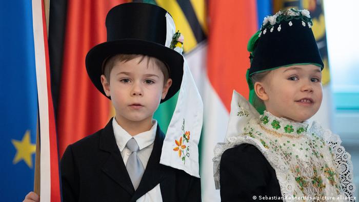 Фотография в традиционных костюмах на фоне флагов ЕС, Германии и Саксонии 