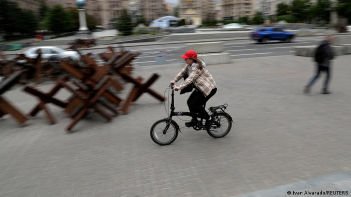 Женщина на складном велосипеде проезжает мимо противотанковых баррикад в центре Киева, 22 мая 2022 года