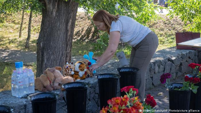 Женщина кладет мягкую игрушку к импровизированному мемориалу у торгового центра Амстор в городе Кремчуг, разрушенного российской ракетой