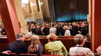 Театральный зал с закрытыми кулисами. Гости ждут открытия фестиваля. Среди них экс-канцлер ФРГ Ангела Меркель